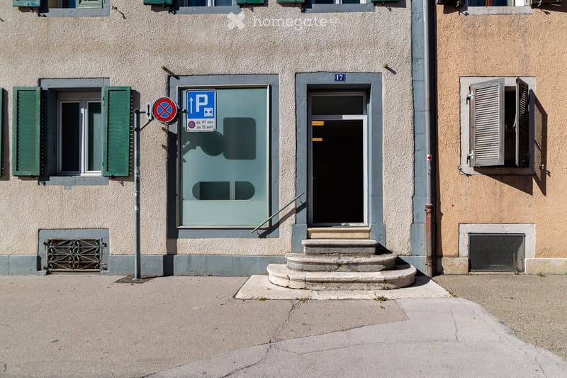 Facade of a multi-story building with a glass door entrance, steps leading up, and a parking sign indicating restricted access.
