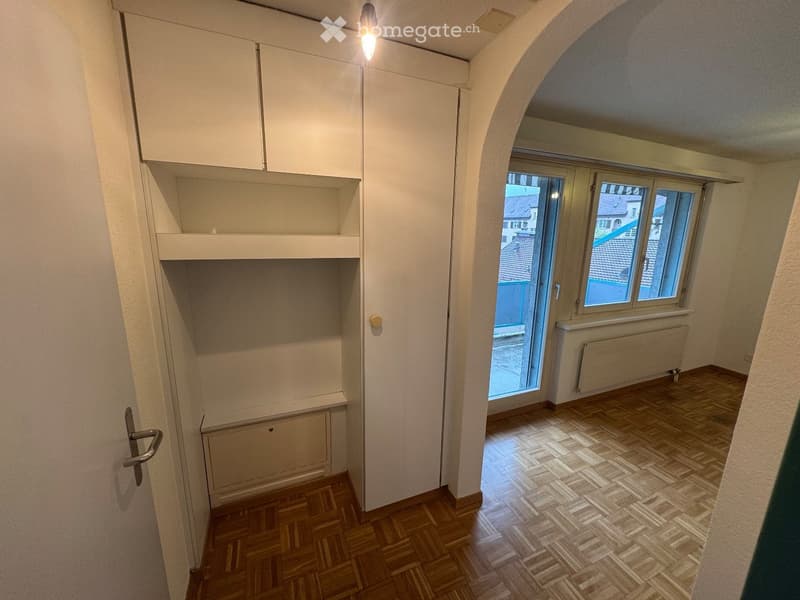 Empty room with wooden flooring, white walls, built-in cabinetry, and a large window with a view of the outside.
