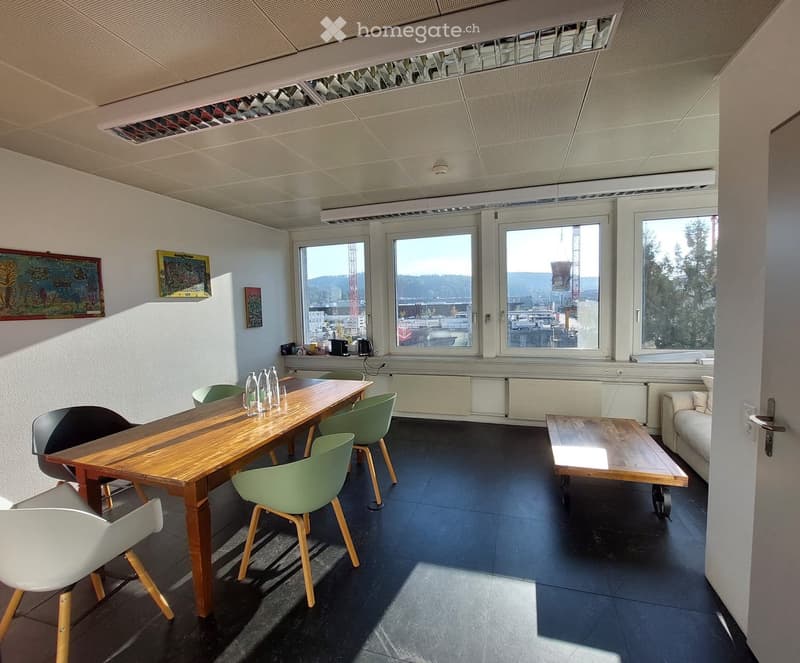 Bright room with large windows, wooden table, green chairs, white chair, small coffee table, and a sofa.