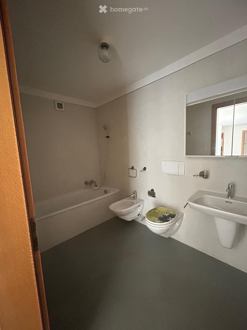 Modern bathroom with a bathtub, toilet, sink, and mirror. Features a sleek design with white fixtures and a dark floor.