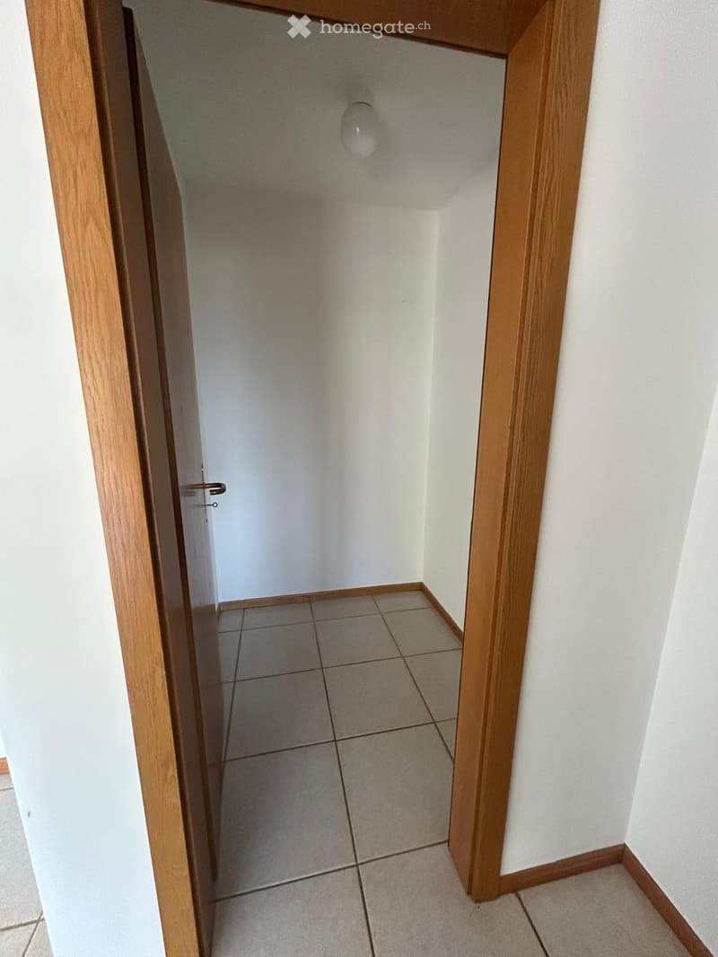 Empty hallway with tiled floor and white walls, featuring a wooden door frame and a light fixture on the ceiling.