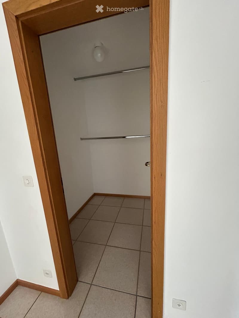 Empty closet with wooden frame, tiled floor, and built-in metal rod for hanging clothes.