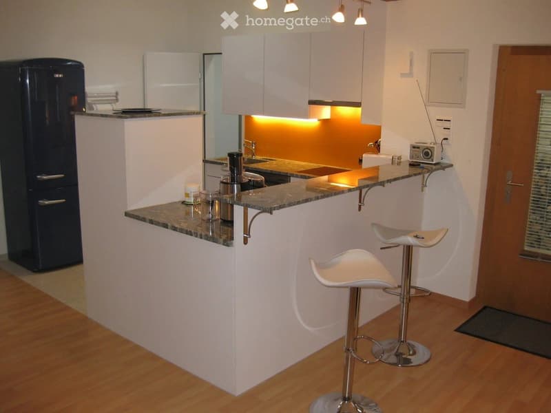 Modern kitchen with white cabinets, granite countertop, stainless steel appliances, and two white bar stools.