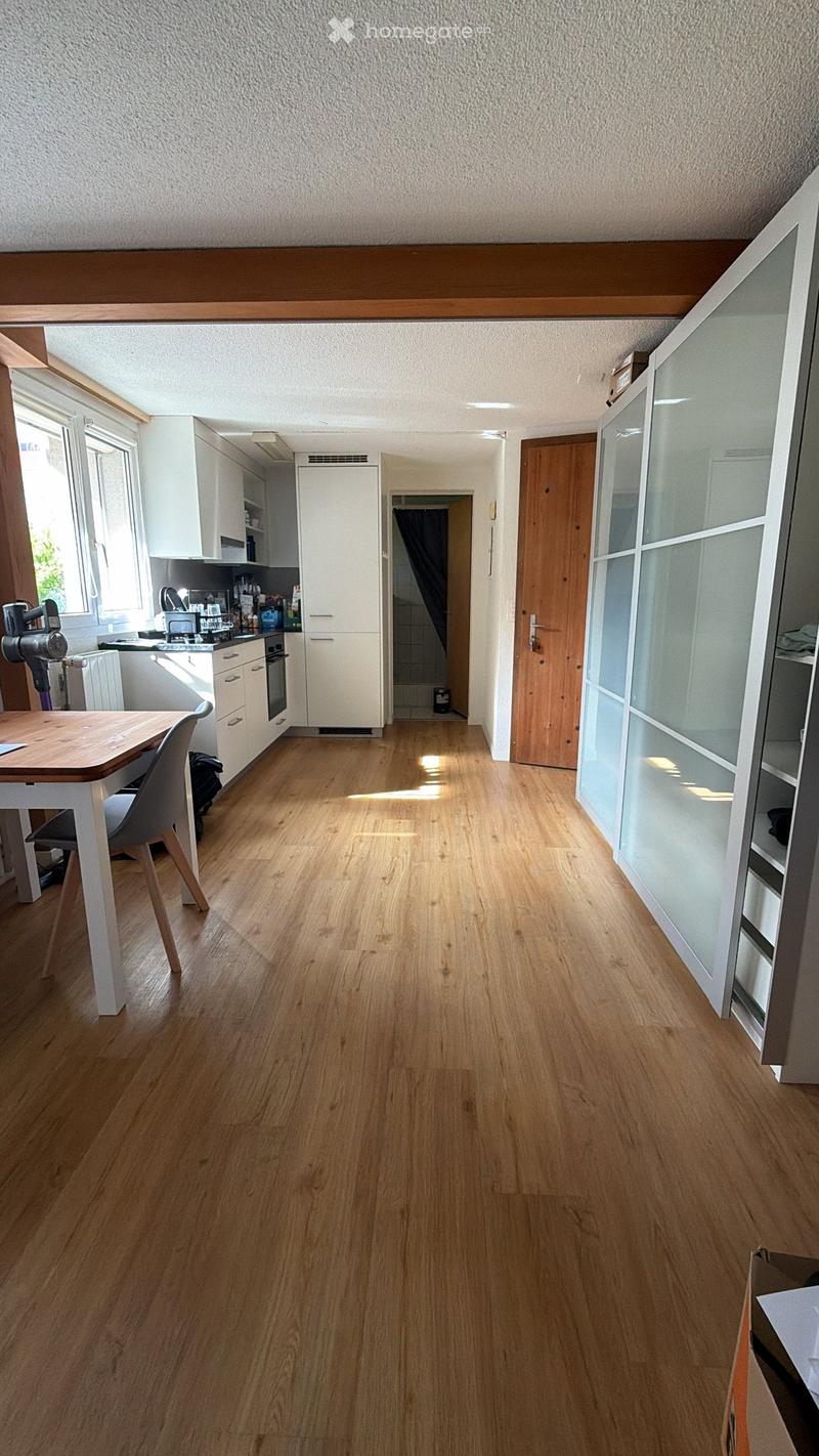 Bright kitchen with light wooden flooring, white cabinets, a small dining area with a table and chair, and a visible oven and faucet.