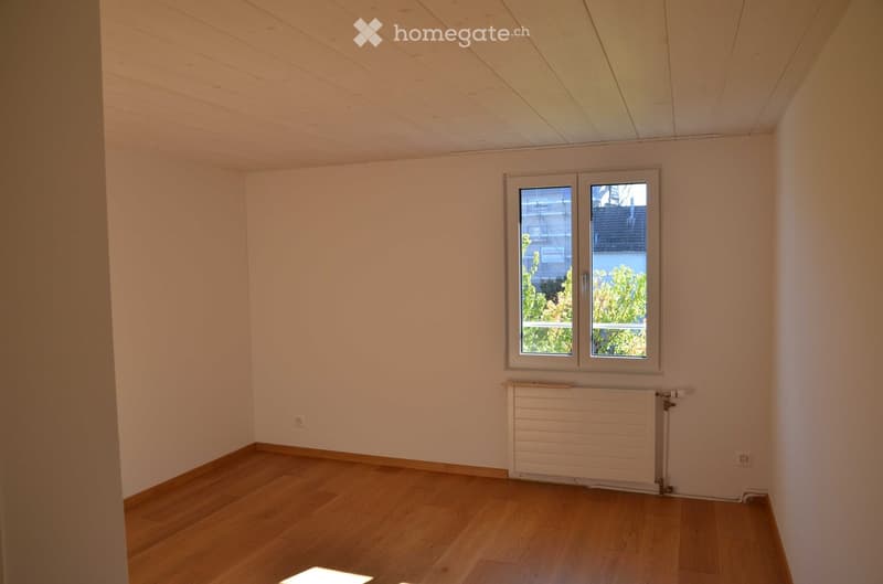 Empty room with wooden flooring, white walls, and a window with a radiator below it.