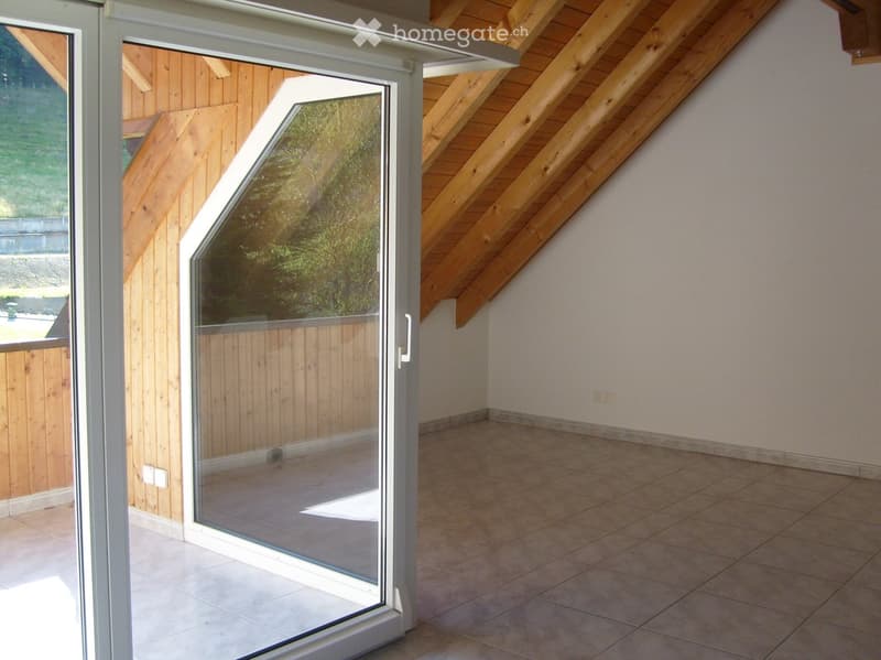 Empty room with tiled floor, white walls, and large sliding glass door leading to an outdoor area with wooden decking and greenery visible.