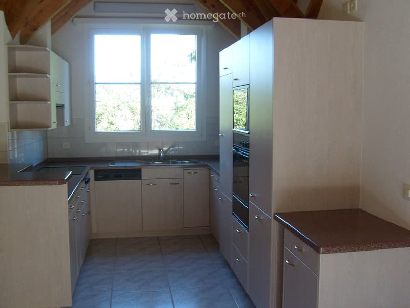 Bright kitchen with light-colored cabinets, a sink, oven, dishwasher, and ample natural light from a large window.