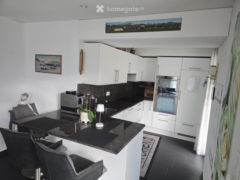 Modern kitchen with white cabinets, black countertop, and stainless steel appliances. Includes a dining area with a table and chairs.