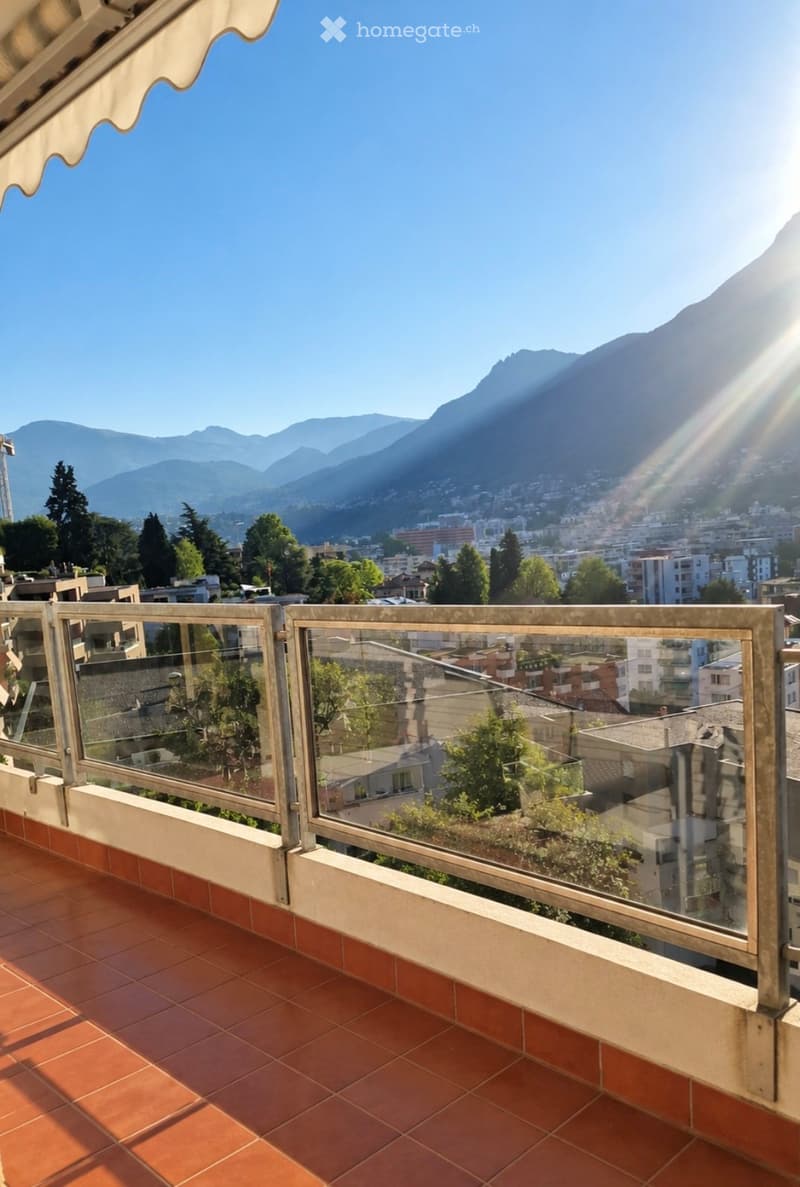 Balcony with glass railing, terracotta tiles, and scenic mountain and city view.