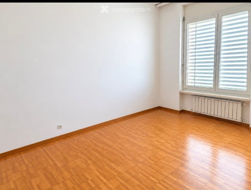 Empty room with wooden flooring, white walls, and large windows with blinds. No furniture or equipment present.