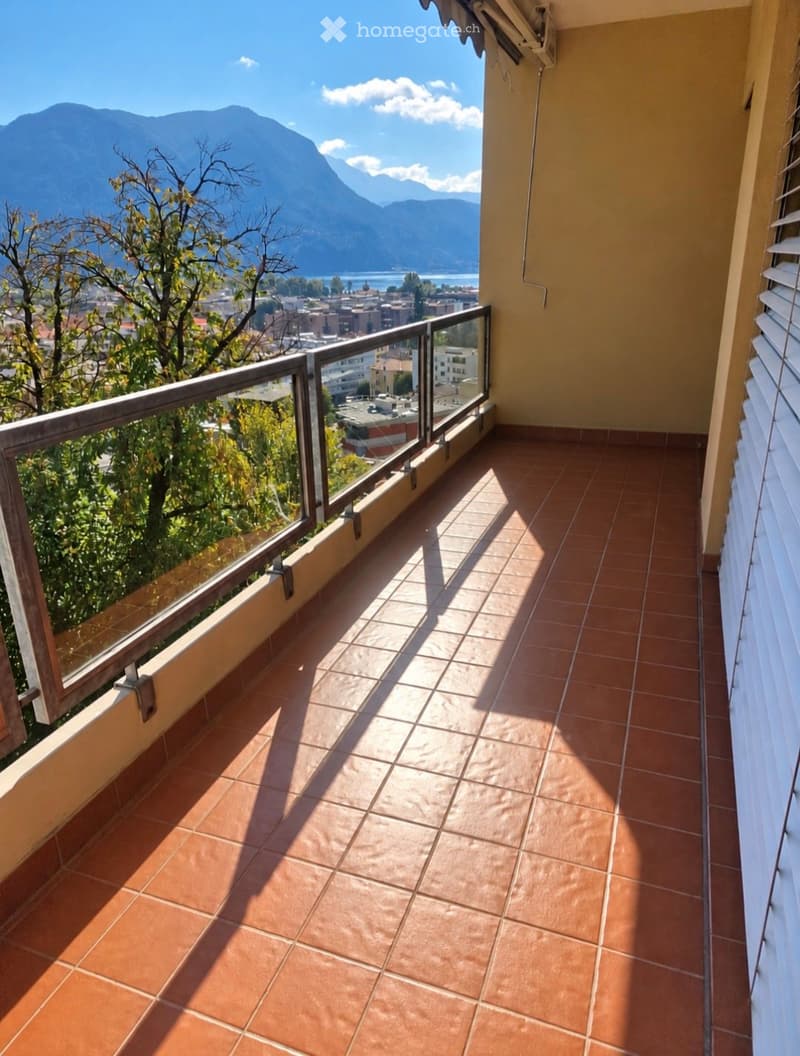 Balcony with terracotta tiles, glass railing, and scenic mountain and city view.