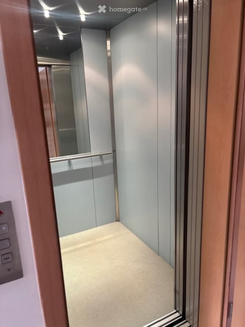Modern elevator interior with light grey walls, a polished floor, and a mirrored ceiling reflecting the lights.