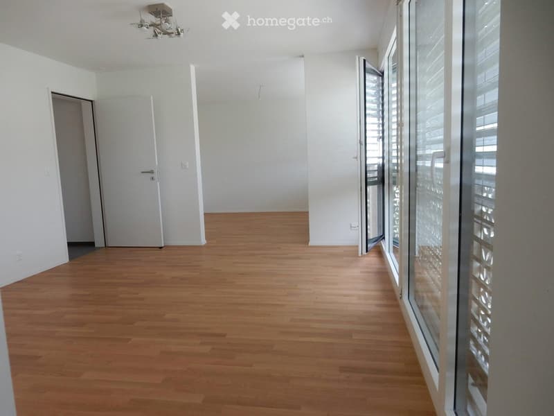Empty room with light wooden flooring, white walls, and large glass windows with blinds. No furniture or equipment present.