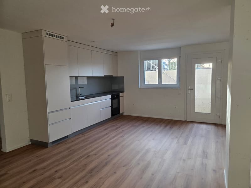 Modern kitchen with light-colored cabinets, a sink, and an oven, featuring wooden flooring and large windows.