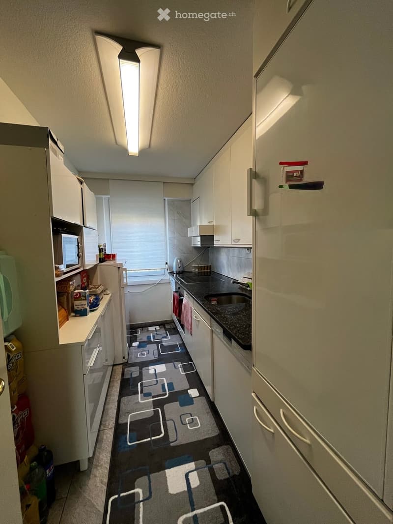 Modern kitchen with white cabinets, dark countertops, and a geometric patterned rug. Features a refrigerator, microwave, sink, and oven.