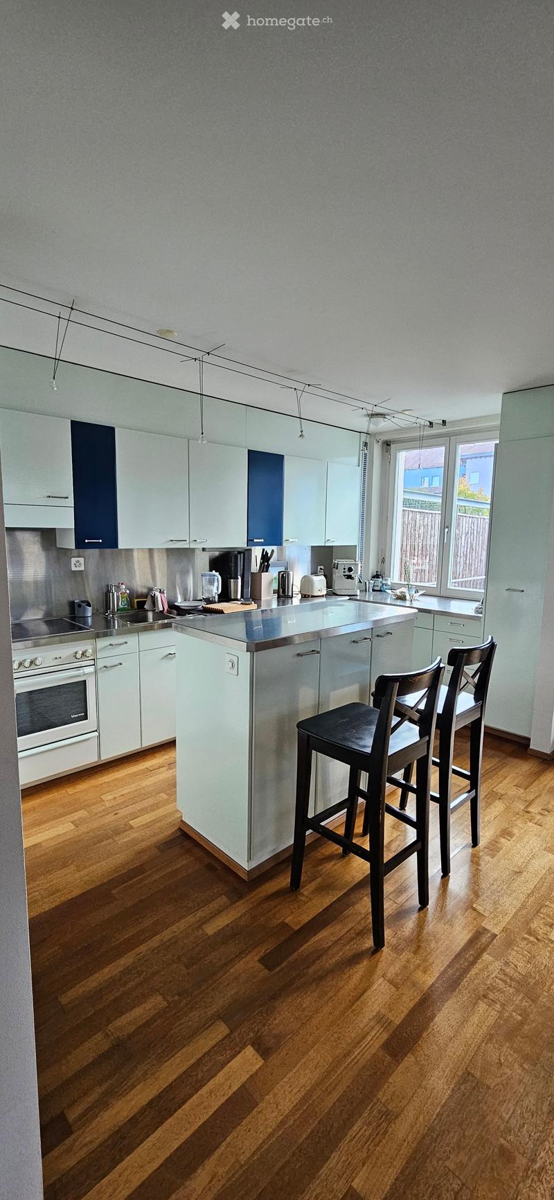 Modern kitchen with light blue cabinets, stainless steel appliances, island, and bar stools.