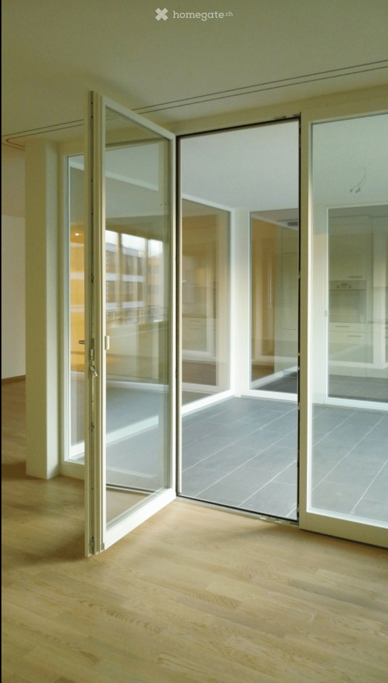Empty room with wooden flooring and large glass sliding doors leading to a tiled outdoor area.