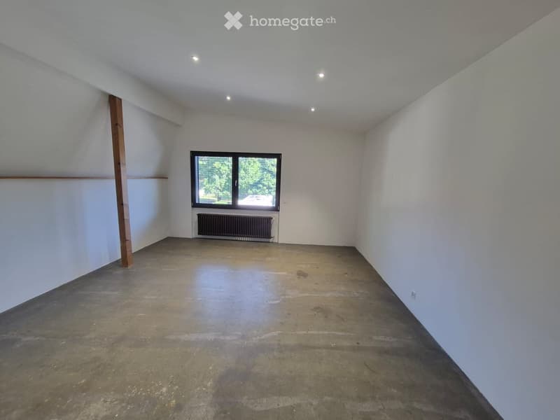 Empty room with white walls, concrete floor, and a single window with black frame. No furniture or equipment present.