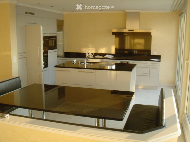 Modern kitchen with white cabinets, black countertops, stainless steel appliances, and a black dining table with stools.