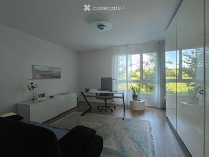 Modern, minimalist room with a sofa, desk, chair, and large windows letting in natural light. The space includes a lamp, a mirror, and a small plant, creating a clean and organized atmosphere.
