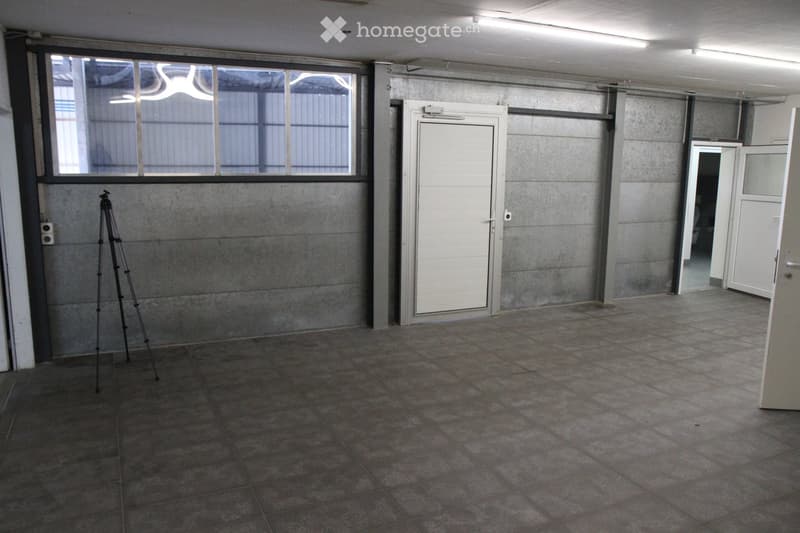 Empty room with concrete walls, tiled floor, large window, and a tripod in the corner.