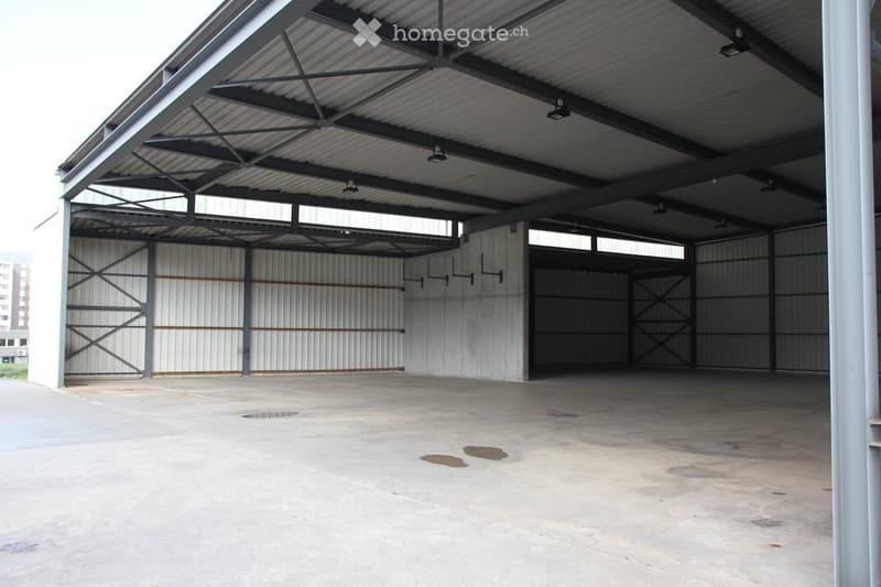 Large industrial-style garage with metal walls, a corrugated metal roof, and multiple large doors. The floor is concrete, and the space is empty with visible structural beams and lighting fixtures.