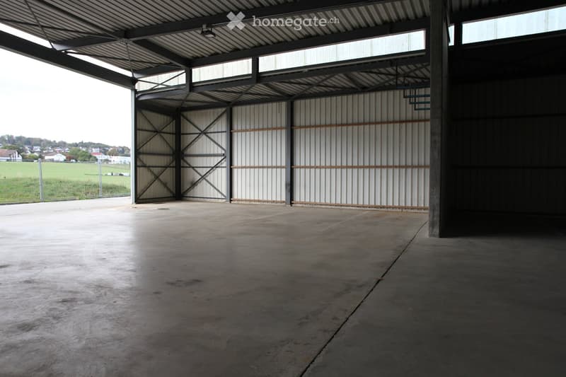 Empty warehouse space with concrete floor, metal walls, large open doors, and a metal roof with skylights.