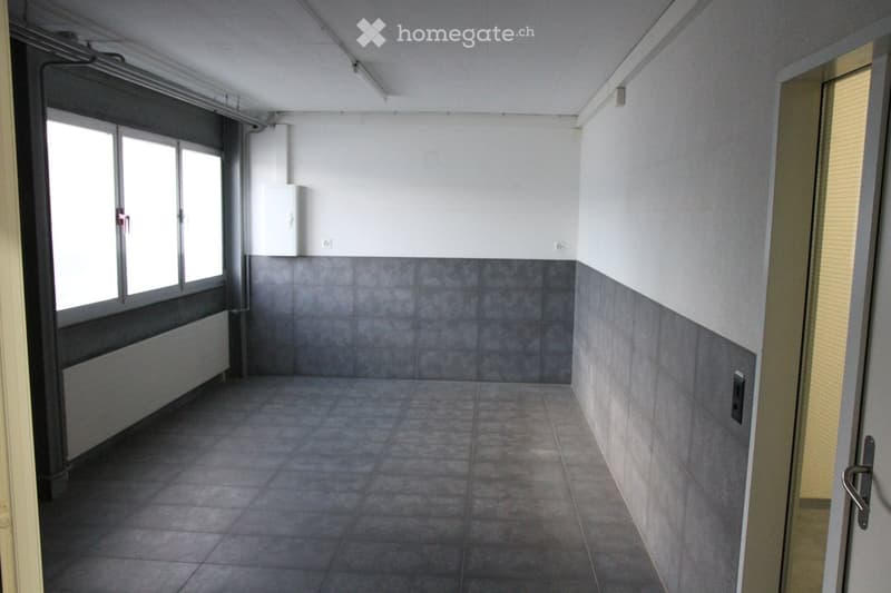 Empty room with tiled floor and walls, large window with blinds, radiator, and a door with a handle.