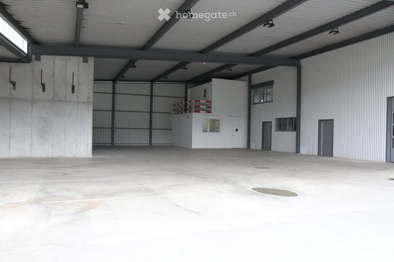 Large industrial warehouse with concrete floors, metal walls, and a raised office area with a balcony overlooking the main space.