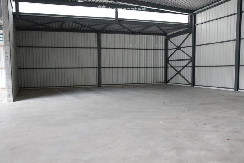 Empty garage with concrete floor, metal walls, and a large open space. No furniture or equipment present.