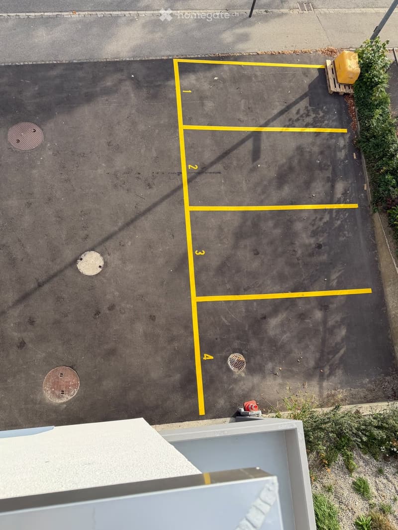 Parking lot with numbered spaces, marked with yellow lines, and a few manhole covers visible.