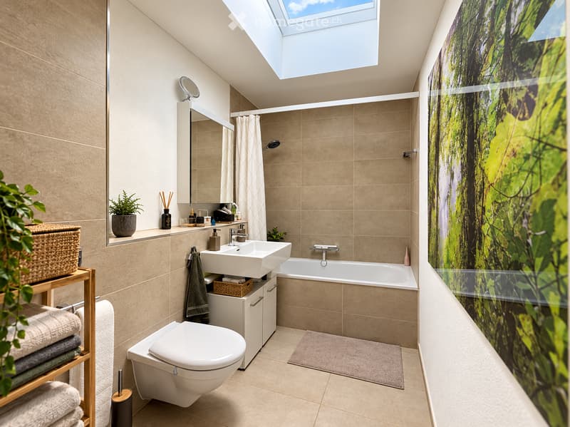 Modern bathroom with a large skylight, beige tiles, a double sink, toilet, bathtub, and a large mirror. Features a wooden shelf with towels and a potted plant, along with a decorative wall mural.