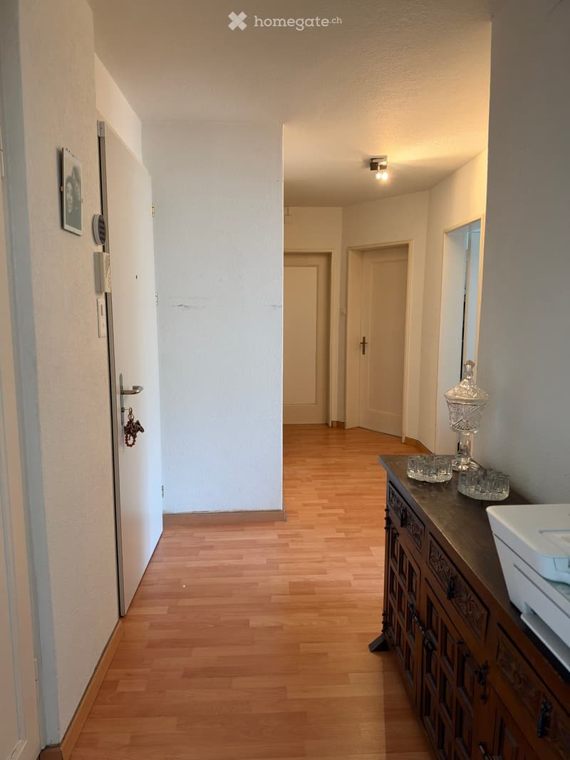 Hallway with wooden flooring, several doors, a small cabinet with a vase and glasses on top, and a picture frame on the wall.
