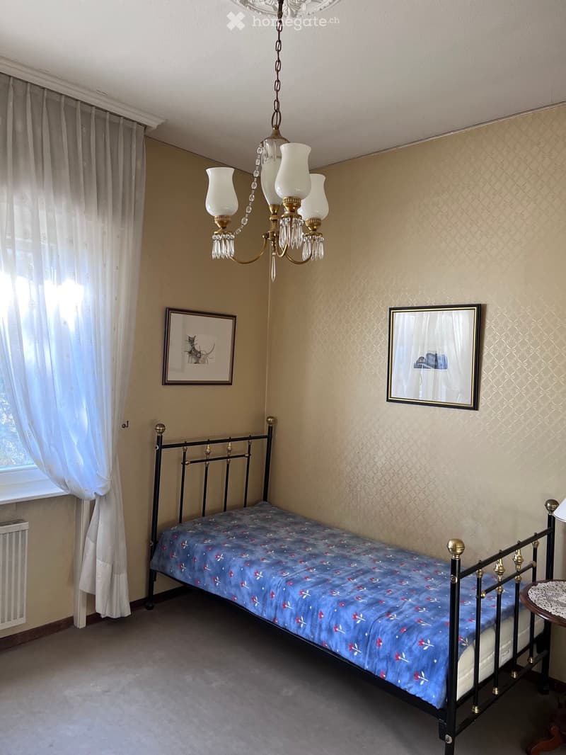 A small bedroom with a single bed, a chandelier, a mirror, and a picture frame on the wall.