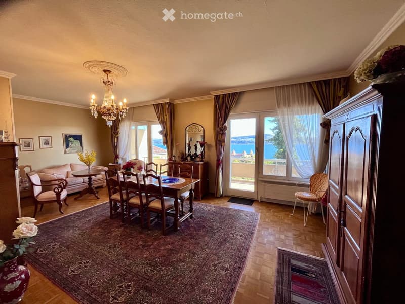 Elegant dining and living area with a large window offering a scenic view, a chandelier, a dining table with chairs, a sofa, and decorative items.