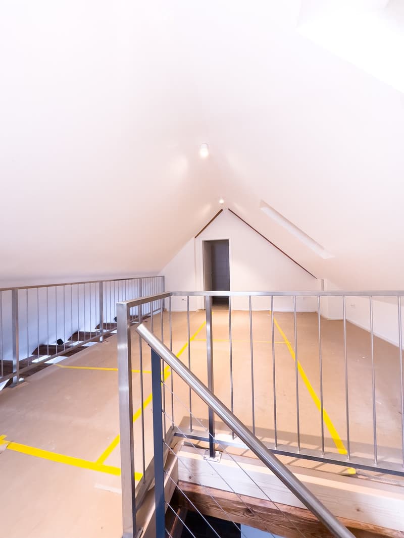 Modern, open staircase with metal railings and wooden steps, leading to an open area with exposed beams and bright lighting.
