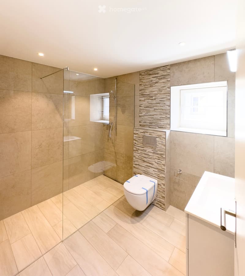 Modern bathroom with beige tiles, glass shower enclosure, toilet, and sink.