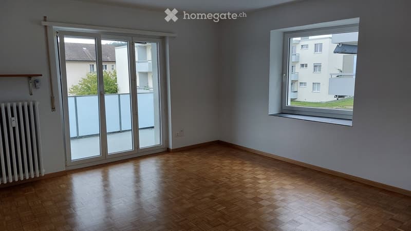 Empty room with wooden flooring, large window, and sliding glass door leading to a balcony.