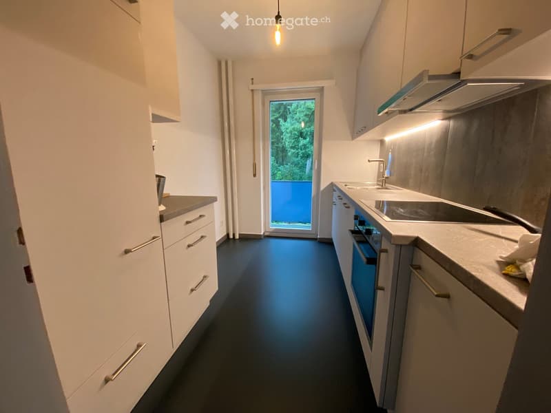 Modern kitchen with white cabinets, stainless steel appliances, and a dark blue floor. Features a sink, faucet, oven, and countertop.