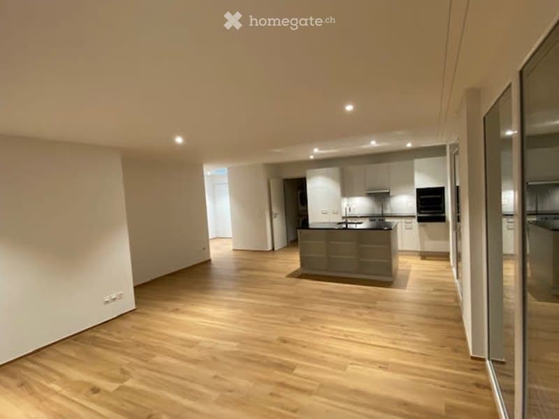 Empty room with a kitchen island, hardwood floors, white walls, and a large window.