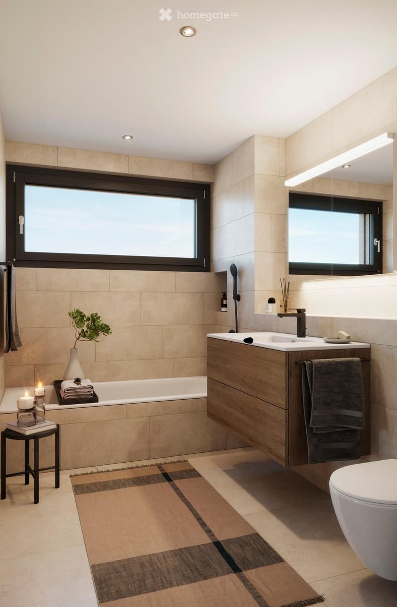 Modern bathroom with beige tiles, a bathtub, a sink with a wooden cabinet, a toilet, a small stool with books and candles, and a plant on the bathtub edge.