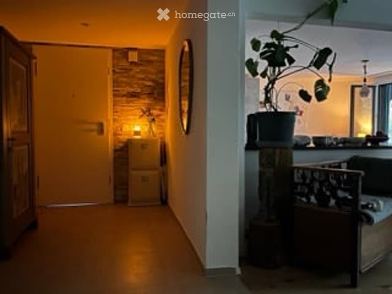A narrow hallway with warm lighting, a small side table with a lamp, and a potted plant on a shelf to the right.
