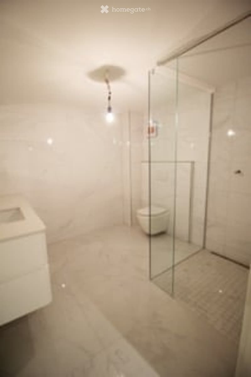 Modern bathroom with white tiles, a glass shower enclosure, a toilet, and a sink.