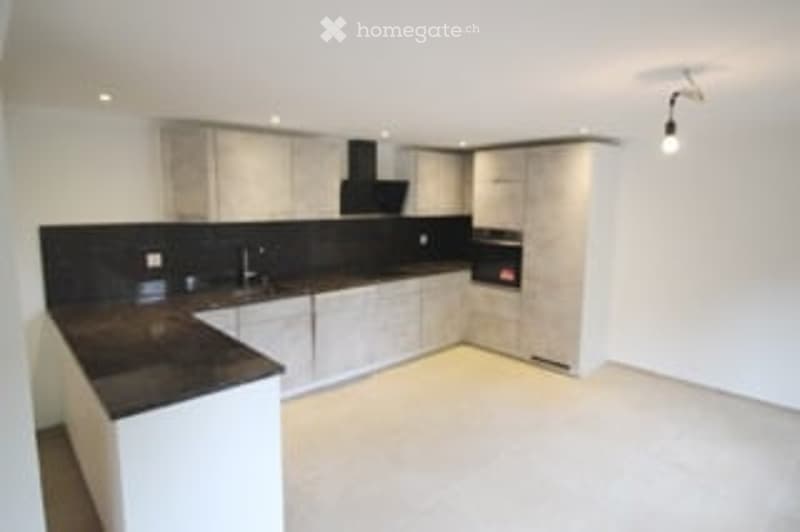 Modern kitchen with white cabinets, black countertops, and a central island. Features a stainless steel sink and a sleek light fixture above.