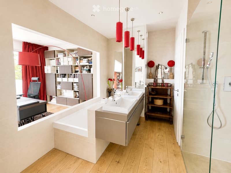 Modern bathroom with double sink vanity, large mirror, built-in cabinets, hanging red lamps, and a glass-enclosed shower area.