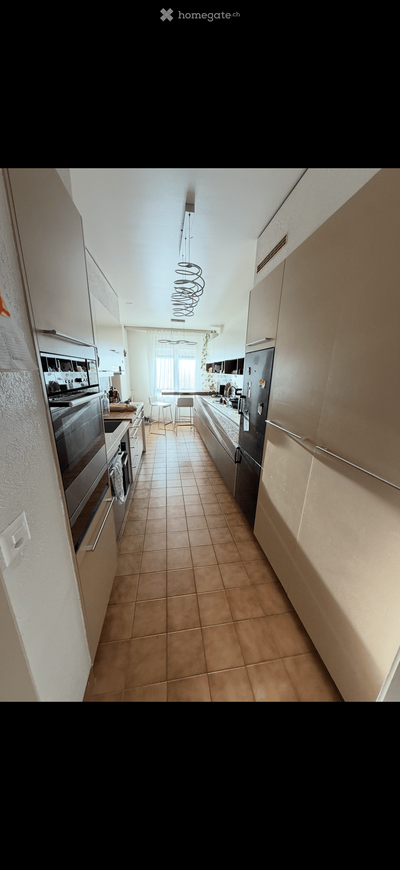 Modern kitchen with light-colored cabinets, stainless steel appliances, tiled floor, and two stools near the island.