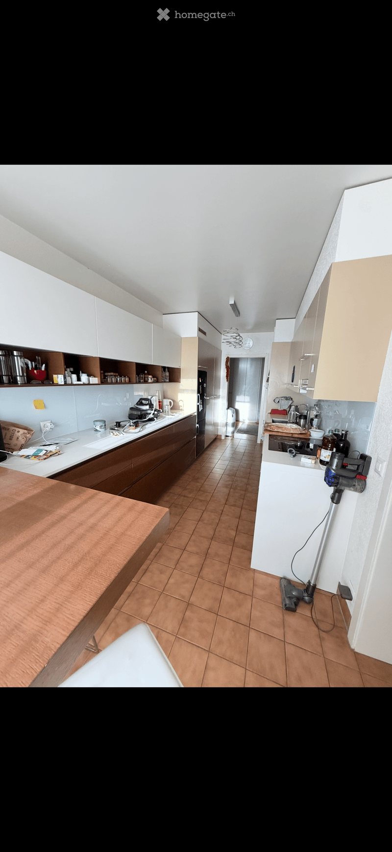 Modern kitchen with white cabinets, wooden countertops, and tiled floor. Includes refrigerator, oven, microwave, dishwasher, coffee maker, toaster, and various kitchen appliances.