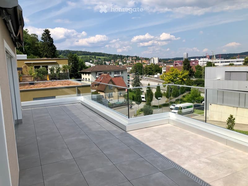 Modern balcony with tiled floor, glass railing, and scenic city view.