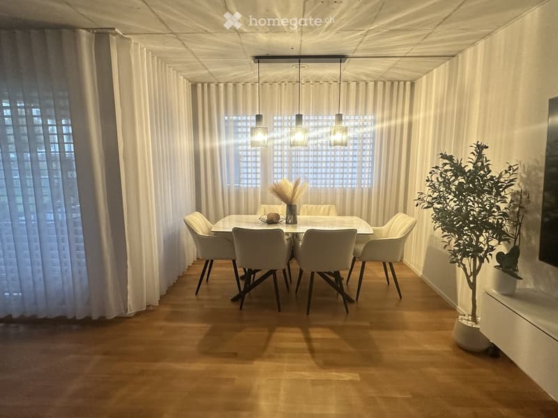 Modern dining room with a white dining table, six chairs, pendant lights, and decorative plants.
