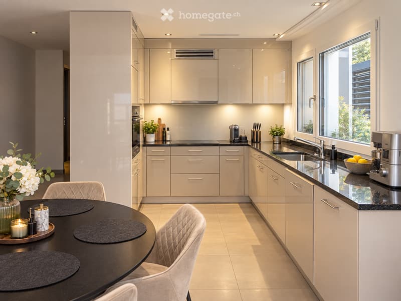 Modern kitchen with white cabinets, black countertops, and a round dining table with chairs. Features include a coffee maker, sink, and decorative items.